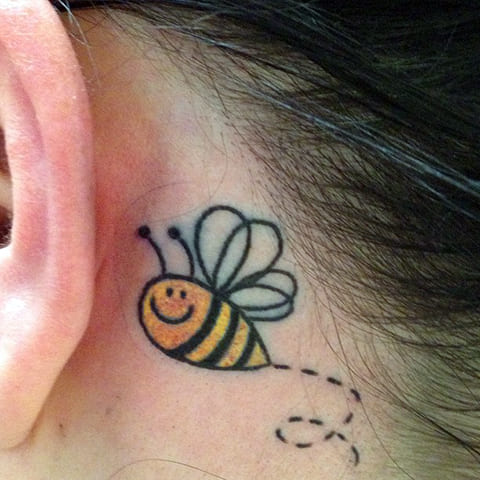 Tattoo of a bee behind the ear