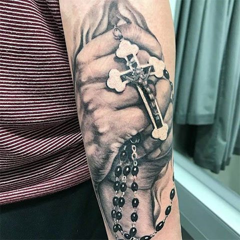 Tattoo of a praying man's hand with a cross