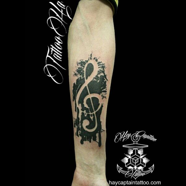 Tattoo of a treble clef as blackwork style notes on the forearm