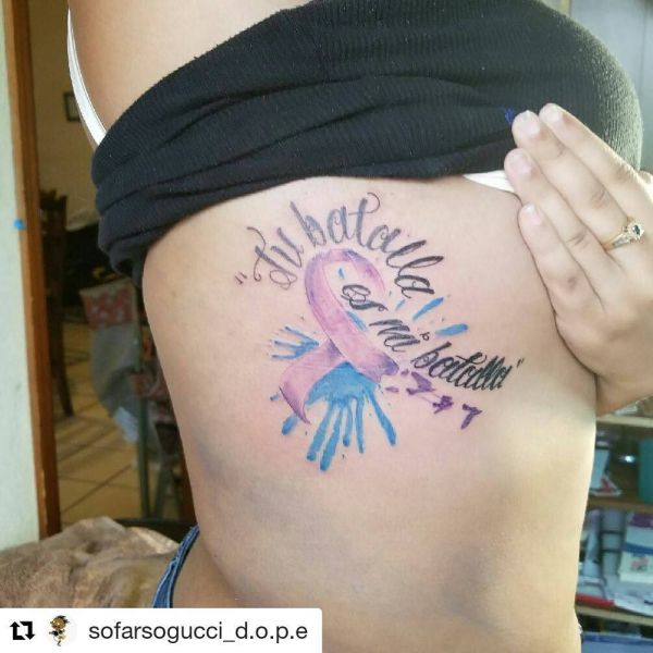 Tattoo in the form of a ribbon and watercolor style inscription on the side of the girl's body