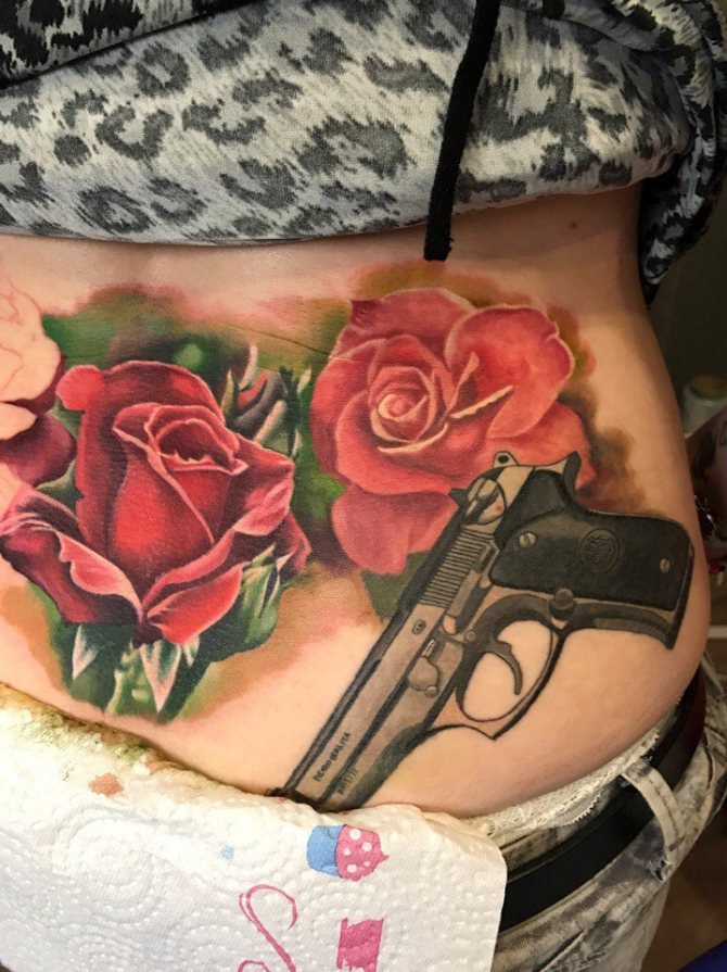 A girl's body tattoo of roses with a gun